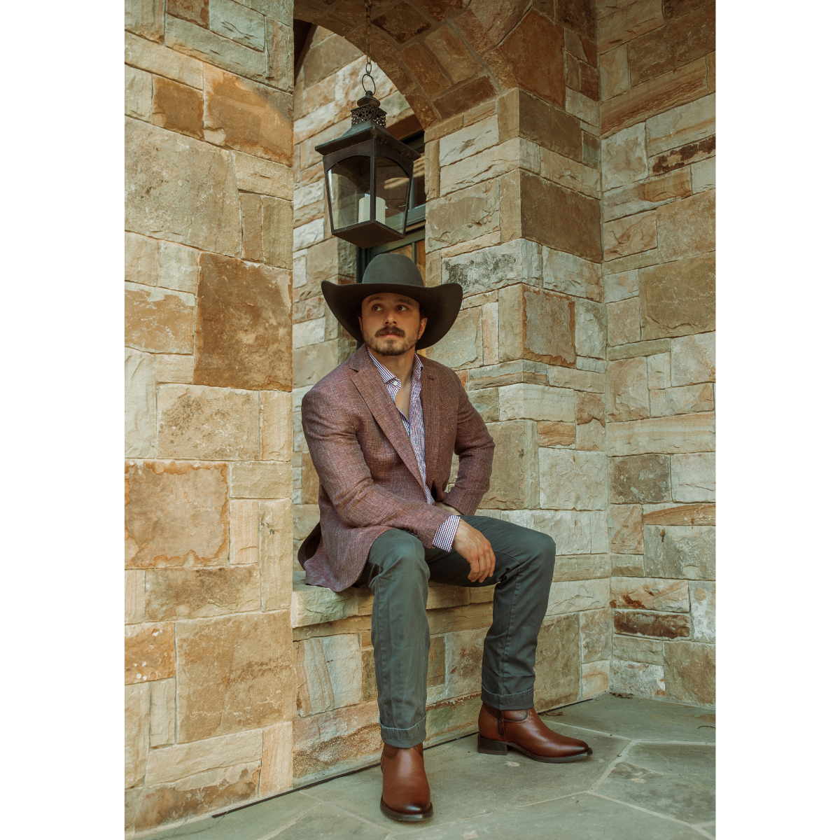 Textured burgundy-brown blazer, olive trousers, brown leather cowboy boots and a dark hat · Río Grande